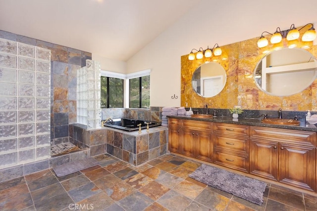 full bath featuring double vanity, a garden tub, stone finish flooring, a sink, and lofted ceiling