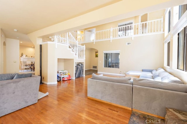 living room with visible vents, arched walkways, a towering ceiling, and wood finished floors