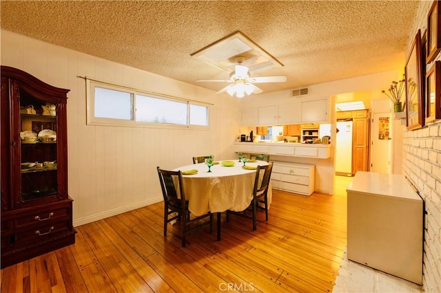 dining space with ceiling fan, light wood finished floors, a textured ceiling, and visible vents