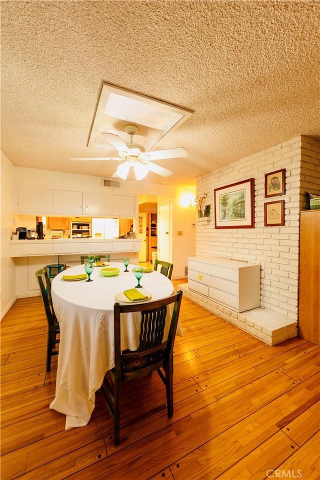 dining room featuring light wood-type flooring, a ceiling fan, a textured ceiling, and visible vents