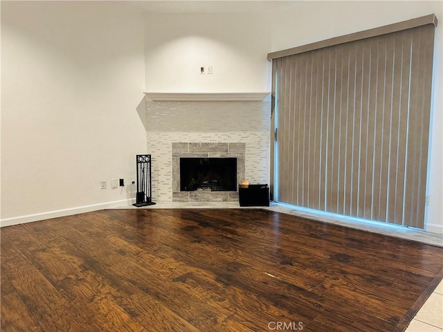 unfurnished living room featuring a tile fireplace, baseboards, and wood finished floors