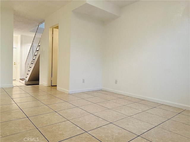 spare room featuring light tile patterned flooring, baseboards, and stairs