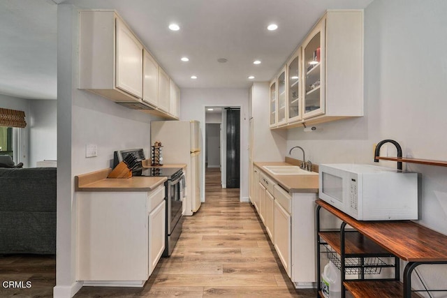 kitchen with a sink, glass insert cabinets, light wood-type flooring, and white appliances