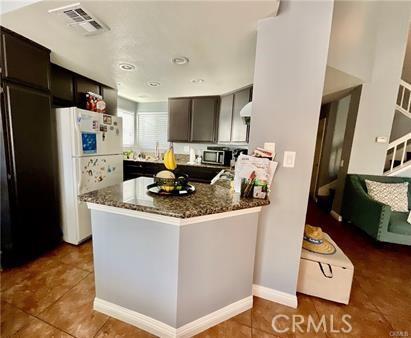 14679 Cinnamon Dr, Fontana, CA 92337 - kitchen with stainless steel microwave, tile patterned flooring, freestanding refrigerator, visible vents, and dark stone counters