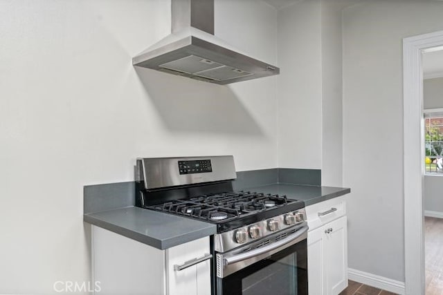 kitchen featuring dark countertops, white cabinetry, stainless steel gas stove, wall chimney exhaust hood, and dark wood-style flooring
