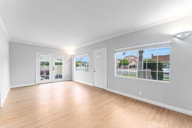 unfurnished living room featuring wood finished floors, crown molding, baseboards, and french doors