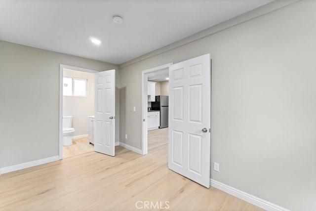 unfurnished bedroom featuring freestanding refrigerator, light wood-style floors, baseboards, and ensuite bathroom