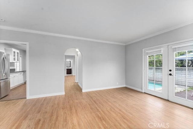 unfurnished living room with arched walkways, baseboards, ornamental molding, and light wood-style flooring