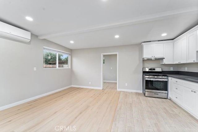 kitchen featuring white cabinets, a wall unit AC, light wood-style floors, gas range, and under cabinet range hood
