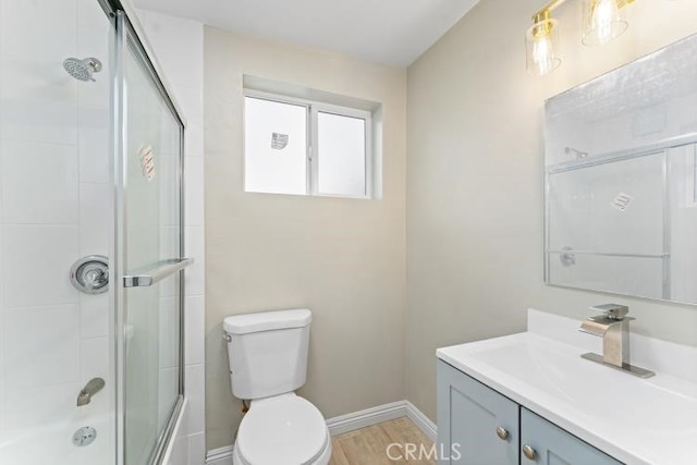 bathroom with wood finished floors, vanity, bath / shower combo with glass door, baseboards, and toilet