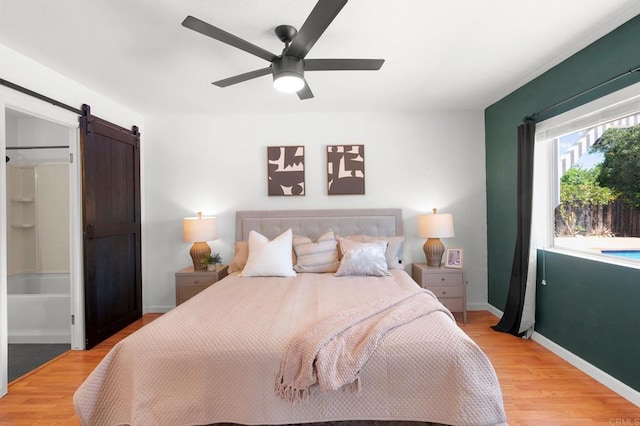 bedroom featuring light wood-style floors, ceiling fan, baseboards, and a barn door
