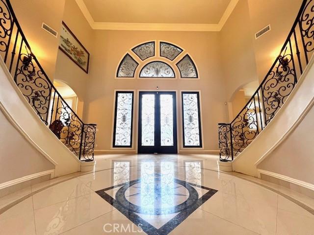 entryway featuring crown molding, marble finish floor, a towering ceiling, and stairs