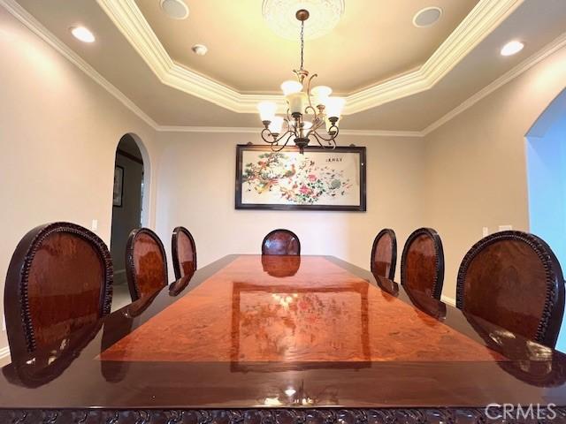 dining room featuring crown molding, a raised ceiling, arched walkways, and a chandelier