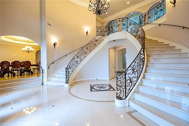 stairway with arched walkways, a towering ceiling, a chandelier, tile patterned flooring, and crown molding
