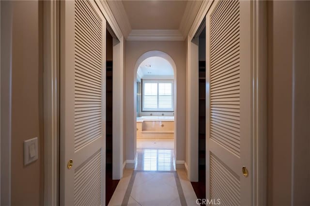 corridor with arched walkways, ornamental molding, and light tile patterned floors