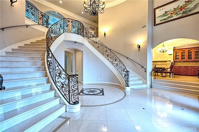 staircase with arched walkways, visible vents, a chandelier, a high ceiling, and crown molding