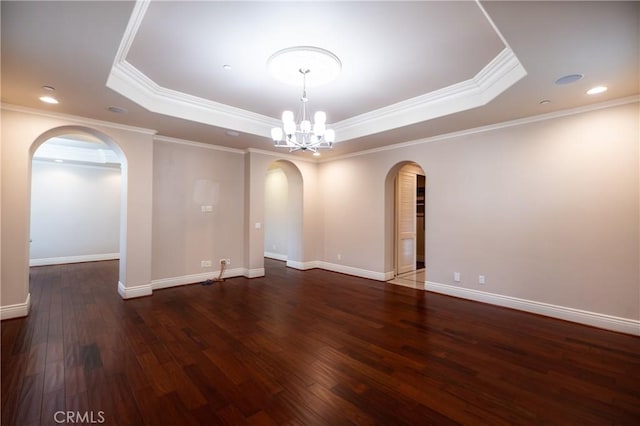empty room featuring an inviting chandelier, a tray ceiling, wood finished floors, arched walkways, and crown molding