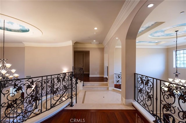 hallway with arched walkways, crown molding, baseboards, and a notable chandelier