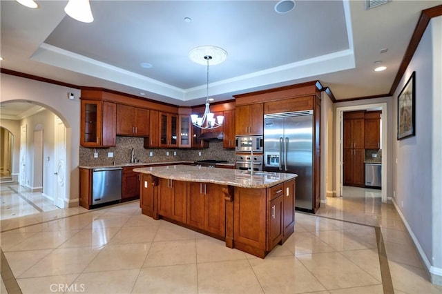kitchen featuring built in appliances, arched walkways, a raised ceiling, and an inviting chandelier