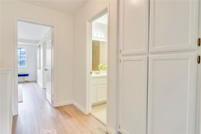 hall with light wood finished floors, baseboards, and a sink