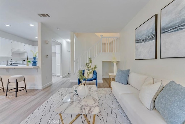 living room featuring recessed lighting, light wood-type flooring, visible vents, and stairs