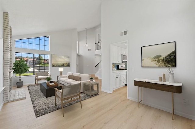 living room with light wood-style floors, high vaulted ceiling, baseboards, and visible vents