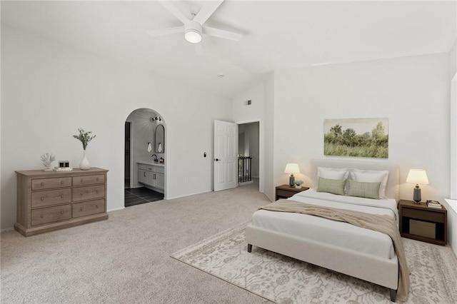 carpeted bedroom featuring arched walkways, ensuite bath, a ceiling fan, vaulted ceiling, and baseboards