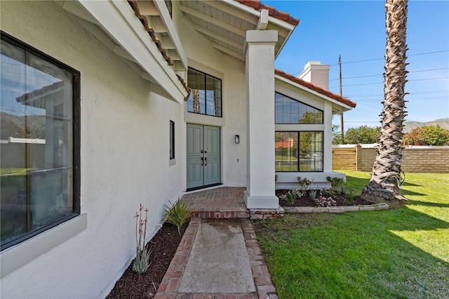 view of exterior entry featuring a chimney, stucco siding, fence, and a yard