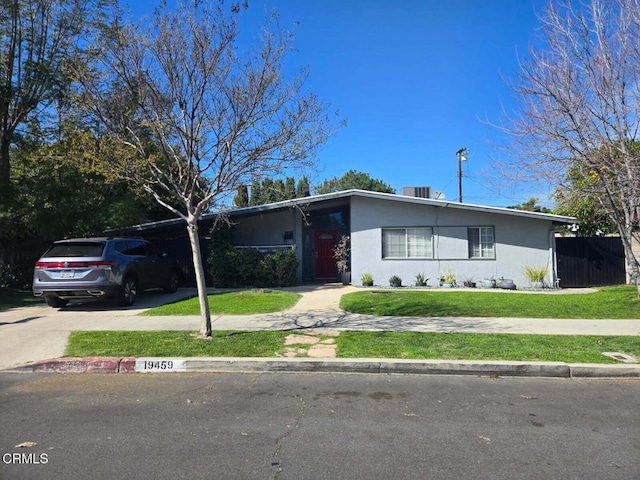 view of front facade featuring stucco siding, driveway, fence, and a front yard