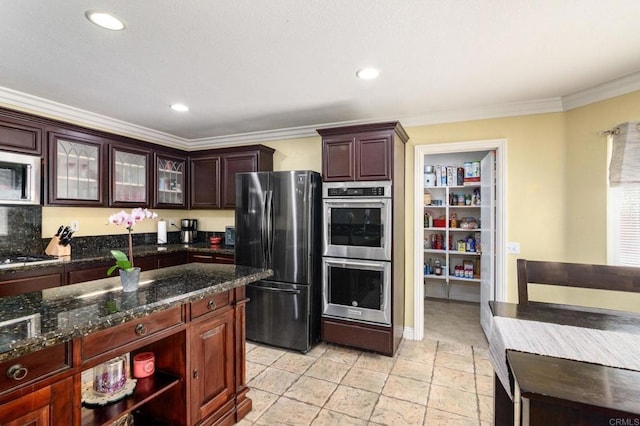 kitchen featuring recessed lighting, ornamental molding, dark stone counters, glass insert cabinets, and appliances with stainless steel finishes