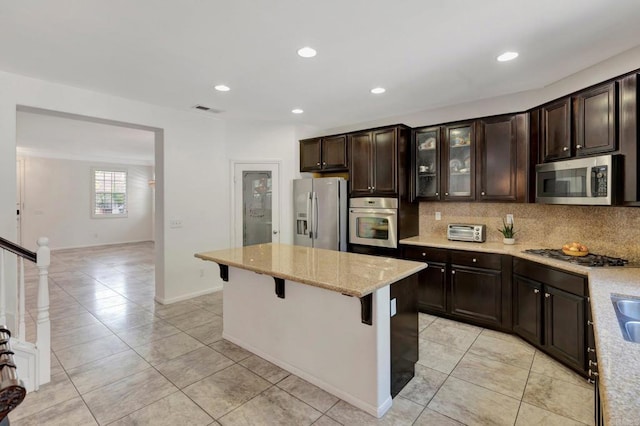 1685 Brezar St, Chula Vista, CA 91913 - kitchen featuring appliances with stainless steel finishes, light tile patterned floors, light stone countertops, a breakfast bar, and a kitchen island