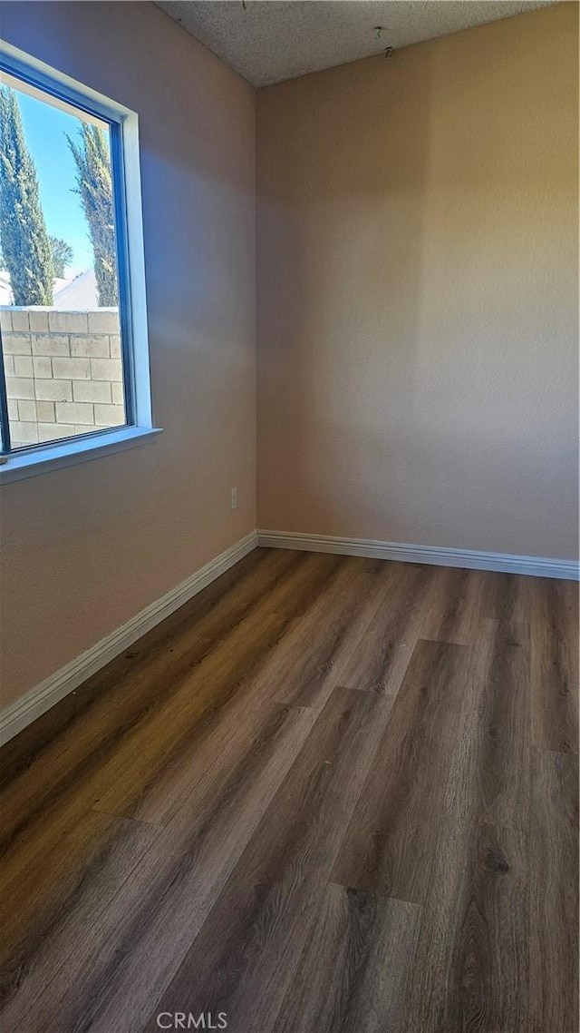 spare room featuring wood finished floors, baseboards, and a textured ceiling