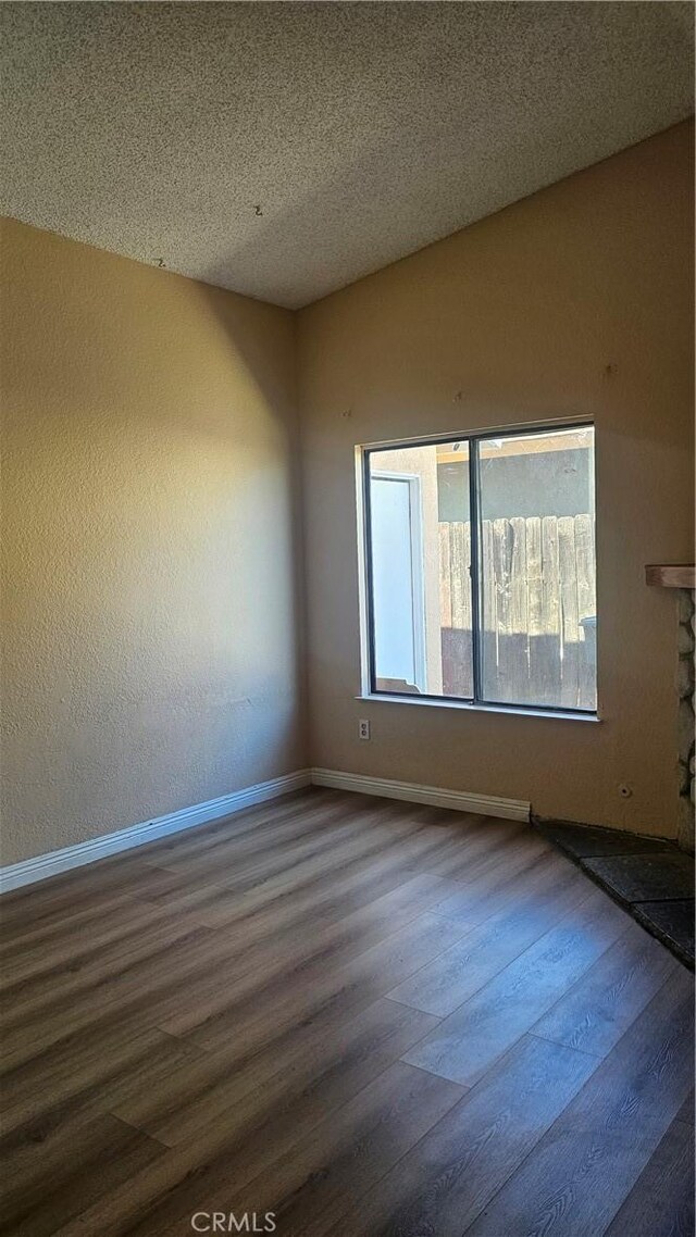 spare room with a stone fireplace, baseboards, dark wood-type flooring, and a textured ceiling