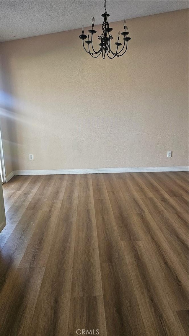 unfurnished dining area with wood finished floors, baseboards, a textured ceiling, and a chandelier