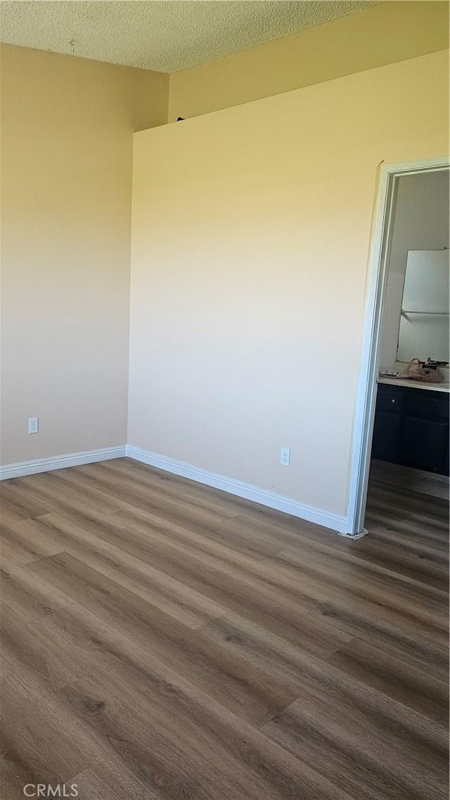 empty room with baseboards, a sink, a textured ceiling, and dark wood finished floors