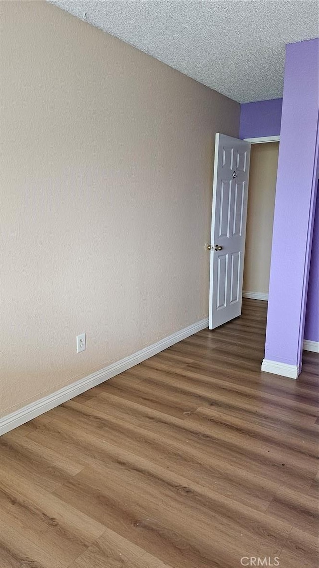 spare room featuring wood finished floors, a textured ceiling, and baseboards