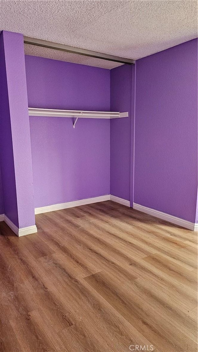 unfurnished bedroom with wood finished floors, a textured ceiling, baseboards, and a textured wall