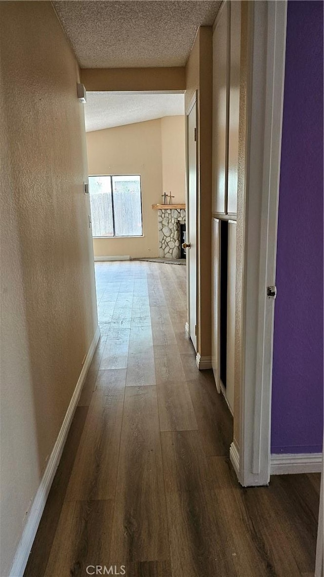 hall featuring baseboards, wood finished floors, and a textured ceiling