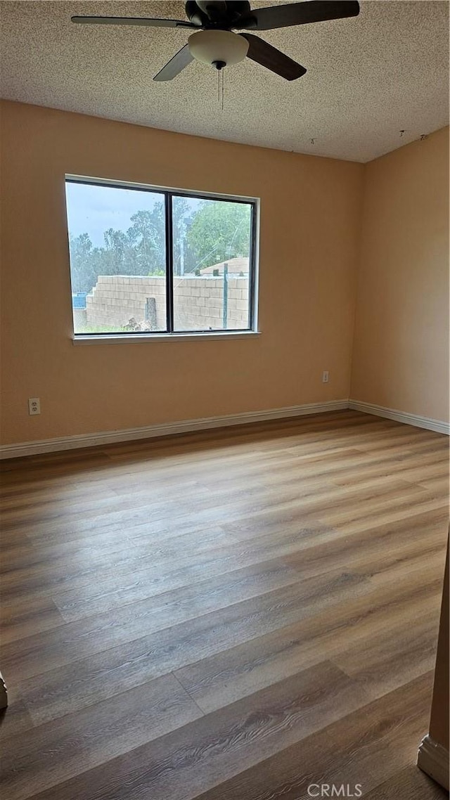 spare room with wood finished floors, a textured ceiling, baseboards, and ceiling fan