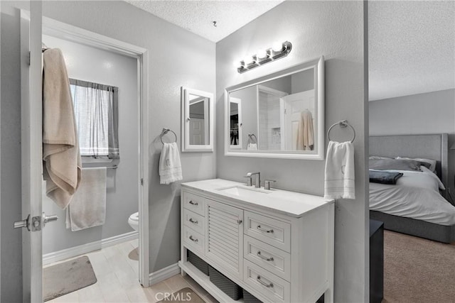 bathroom with a textured ceiling, vanity, baseboards, toilet, and ensuite bath