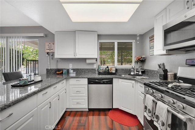 kitchen featuring white cabinets, appliances with stainless steel finishes, a sink, dark stone countertops, and dark wood-type flooring