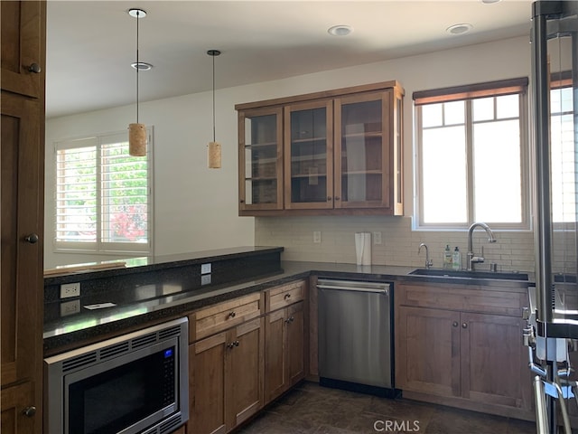 kitchen with glass insert cabinets, stainless steel appliances, backsplash, a sink, and pendant lighting