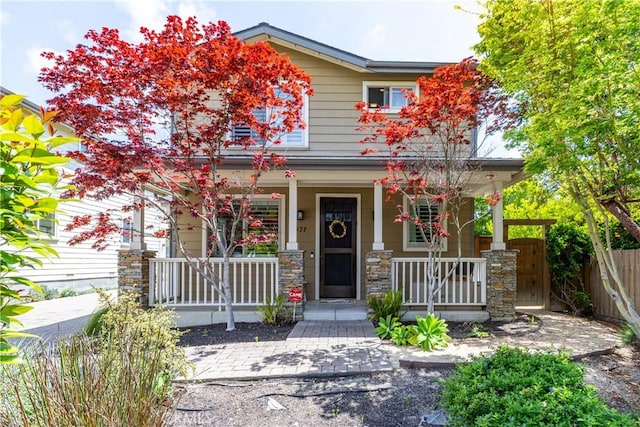 view of front of property featuring a porch, stone siding, and fence