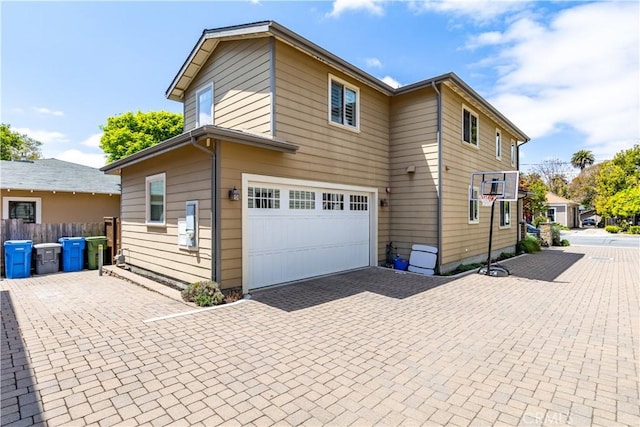 view of side of property with decorative driveway, an attached garage, and fence