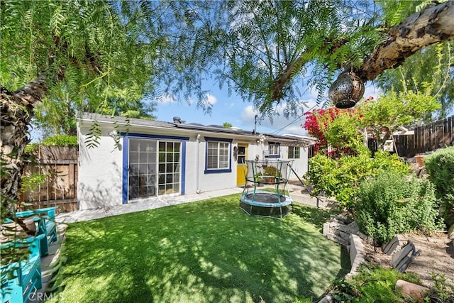 rear view of property with roof mounted solar panels, stucco siding, fence, and a lawn