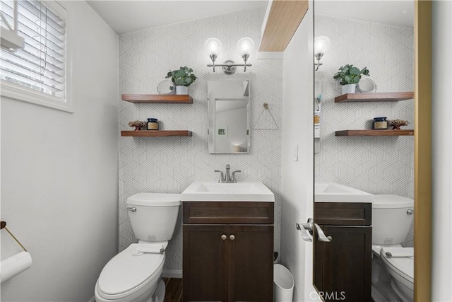 half bath with toilet, wallpapered walls, and vanity