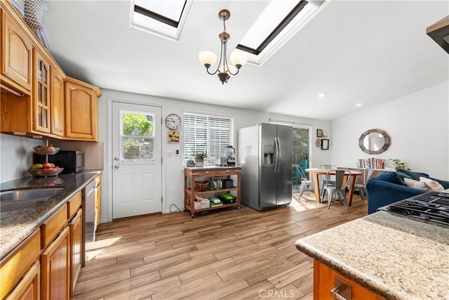 kitchen featuring glass insert cabinets, brown cabinetry, light stone counters, stainless steel appliances, and light wood finished floors