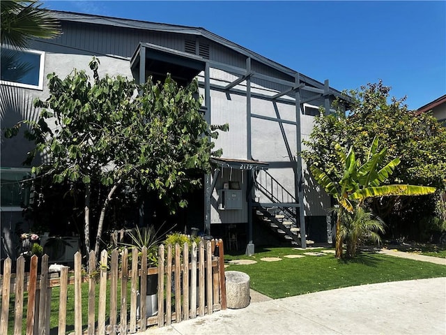 view of home's exterior featuring fence, a lawn, and stairs