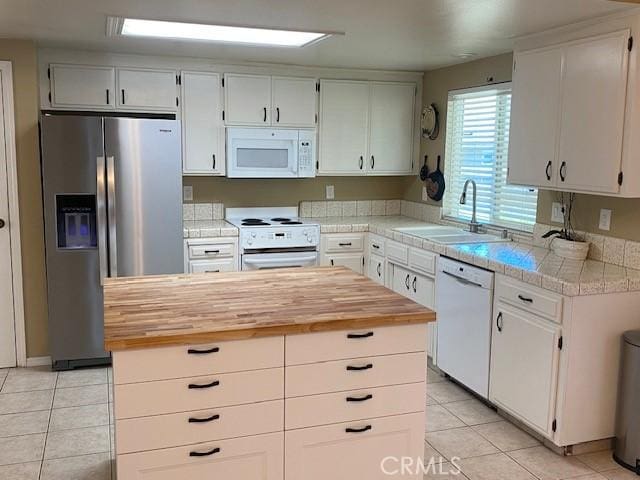 kitchen featuring butcher block countertops, light tile patterned flooring, a sink, and white appliances