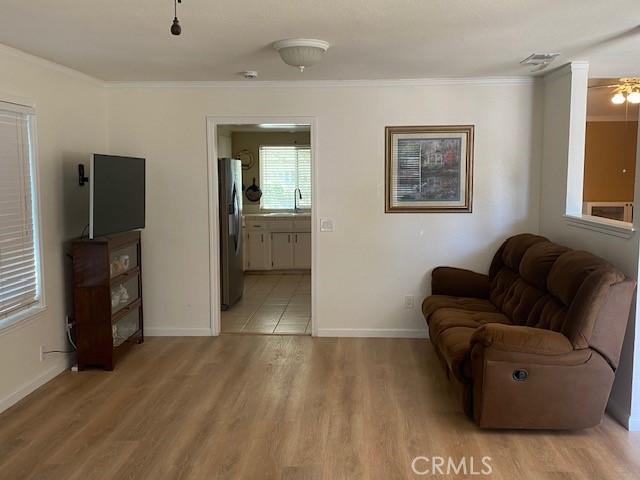 living room featuring visible vents, ornamental molding, light wood-style flooring, and baseboards